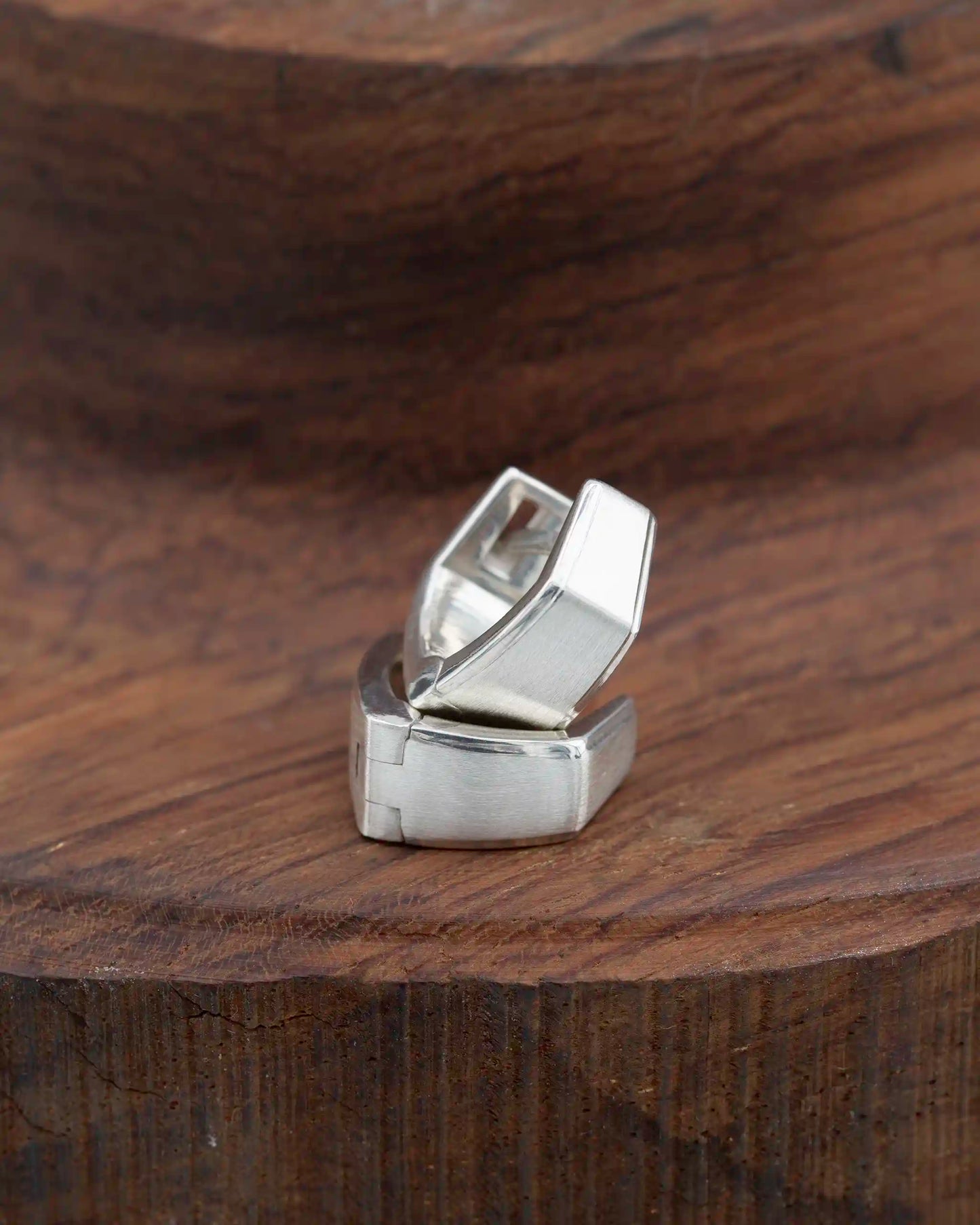 Stylish geometric silver huggie earrings with a contemporary design, displayed on a textured wooden surface.