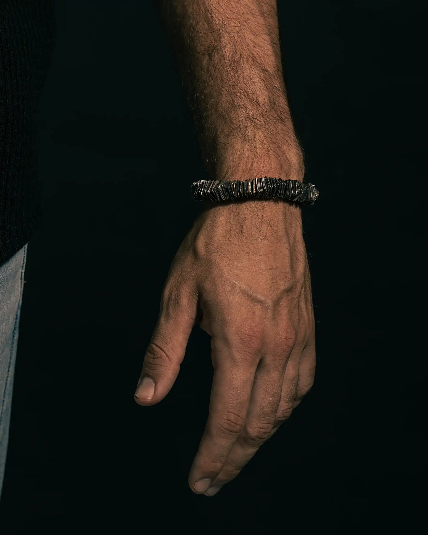 Hand wearing the 'Hundred Plates' bracelet, showcasing layered silver detailing and rugged design.