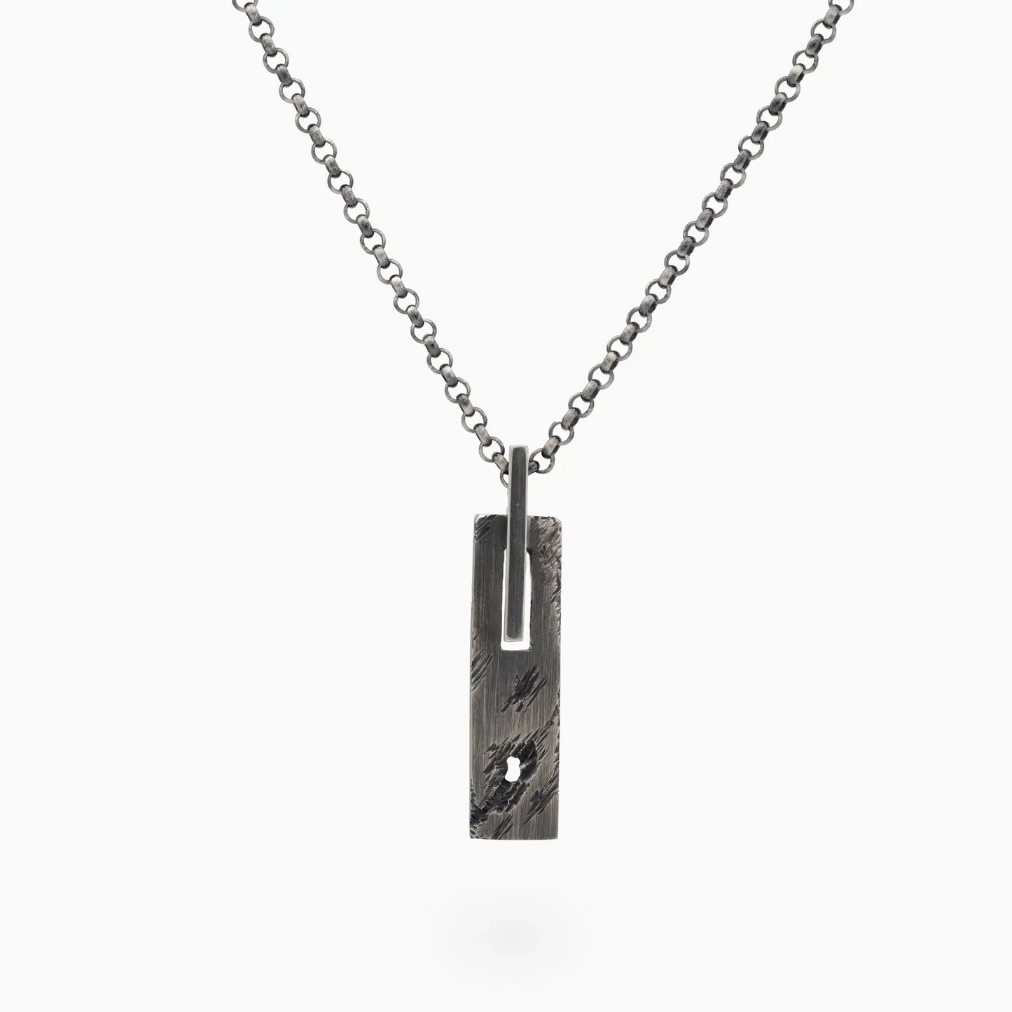 A silver chain necklace with a rectangular, textured pendant featuring a small hole and an attached metal loop.