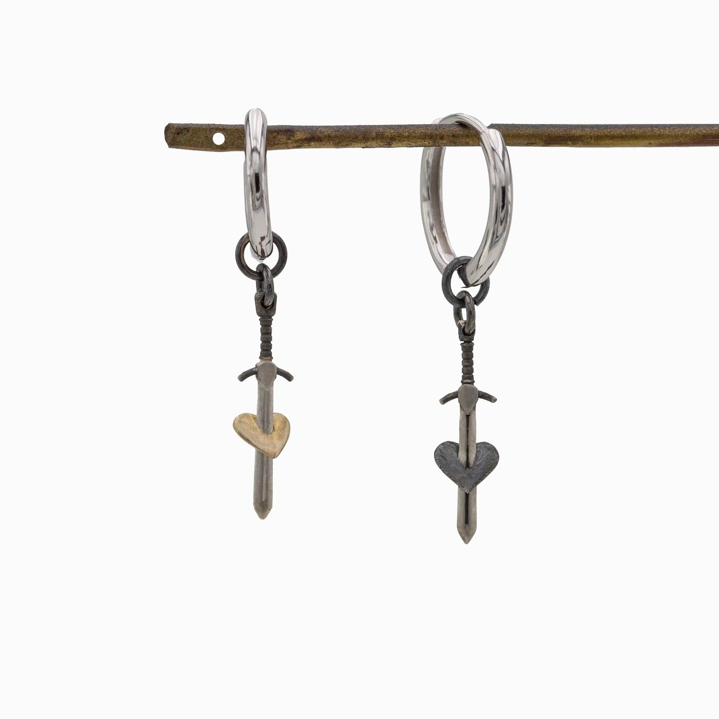Pair of sterling silver hoop earrings with sword and heart pendants, one gold heart and one black heart, handmade jewelry