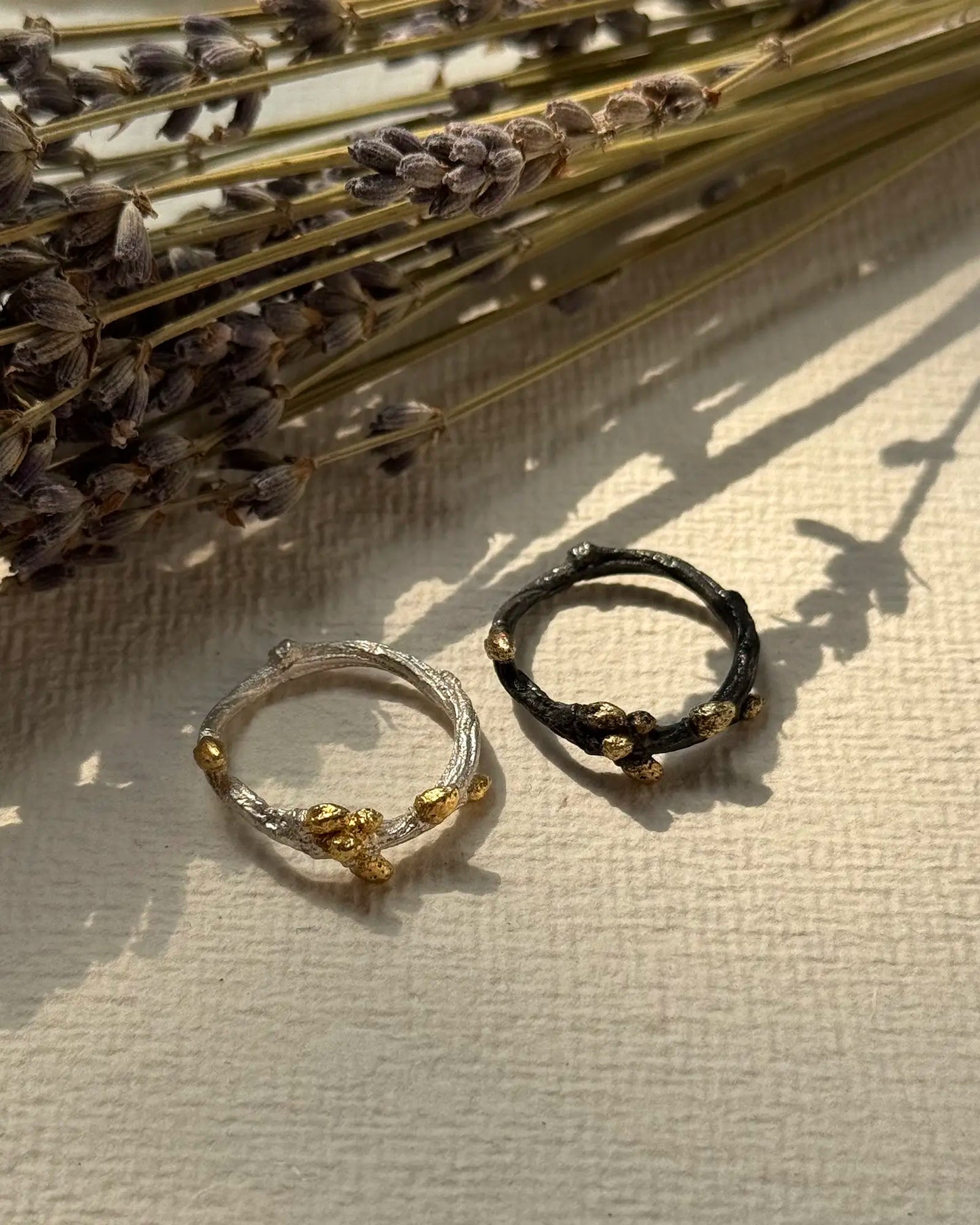 Two handmade SteelWaters Bonsai rings in sterling silver and oxidized black finish with gold accents, styled with dried lavender