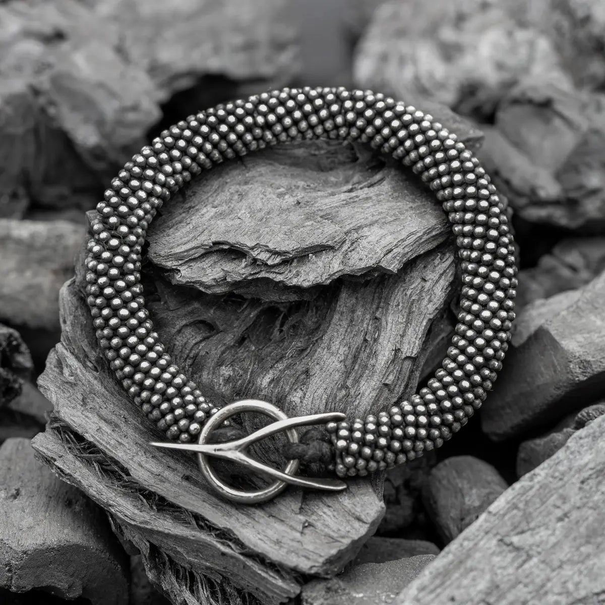 A handcrafted silver bead bracelet with a minimalist clasp, set against weathered wood and stone.