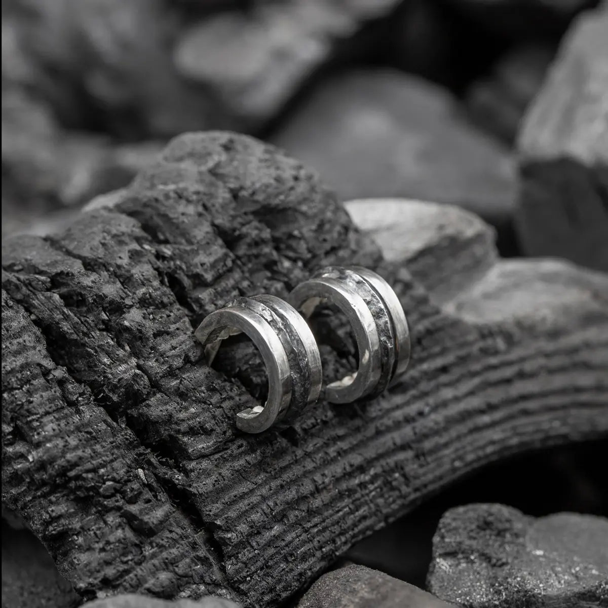 Hammered silver hoop earrings on a textured, charred wood surface.