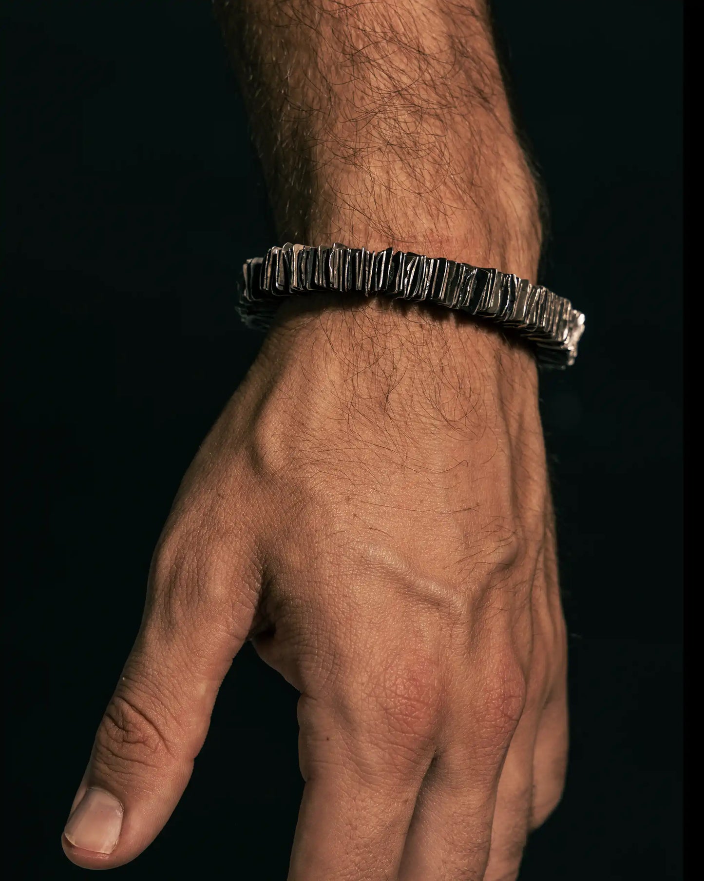Rugged handcrafted silver bracelet with layered metal plates, worn on a male wrist against a dark background.