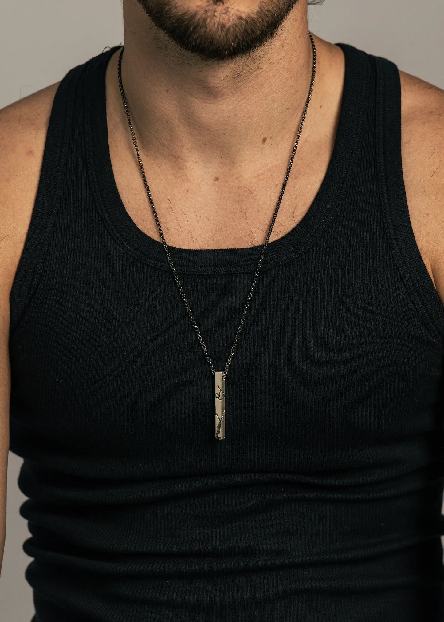 Sterling silver man wearing a lightning-inspired pendant on a black chain, paired with a casual tank top.