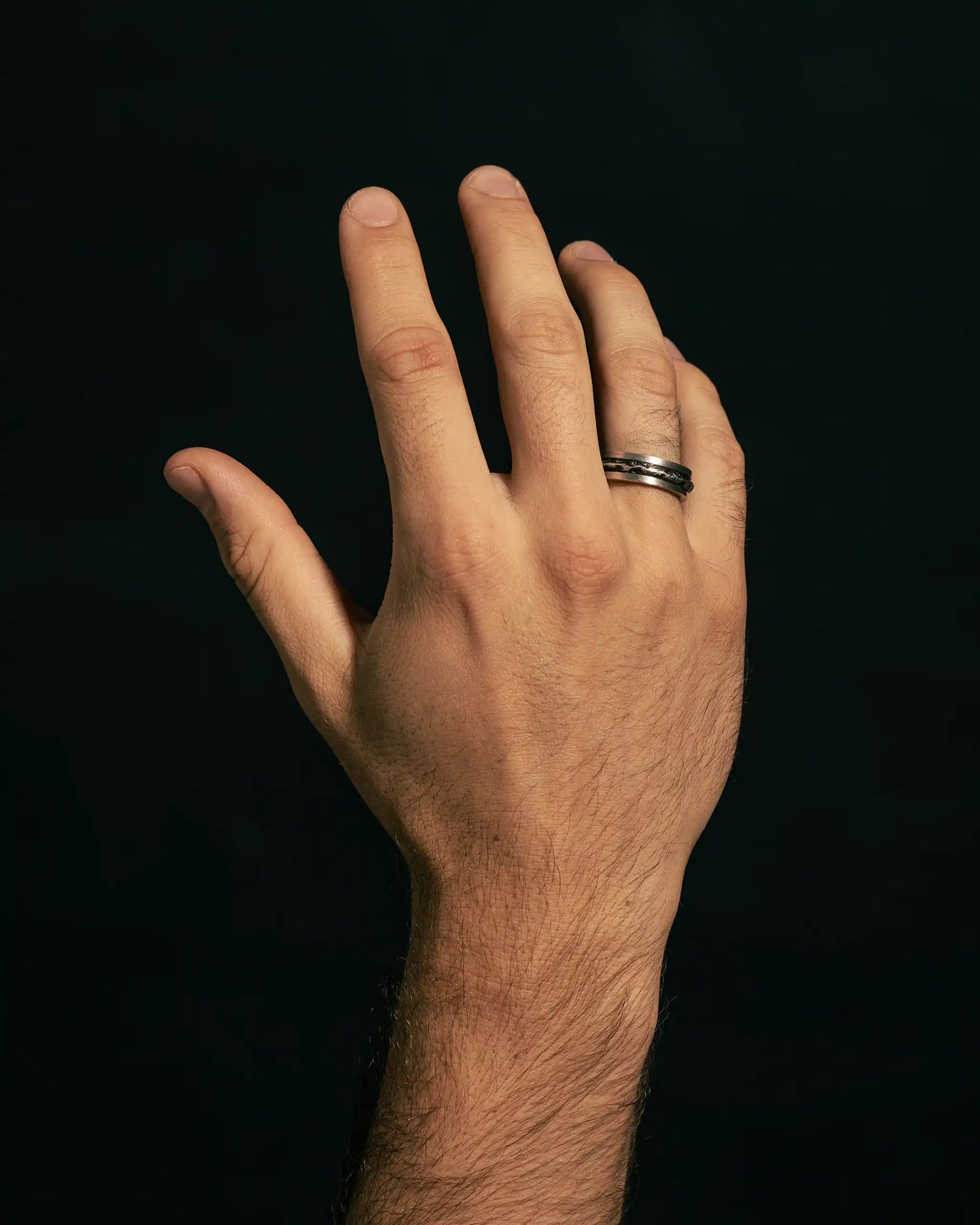 Hand wearing a silver mountain-inspired ring with textured details.