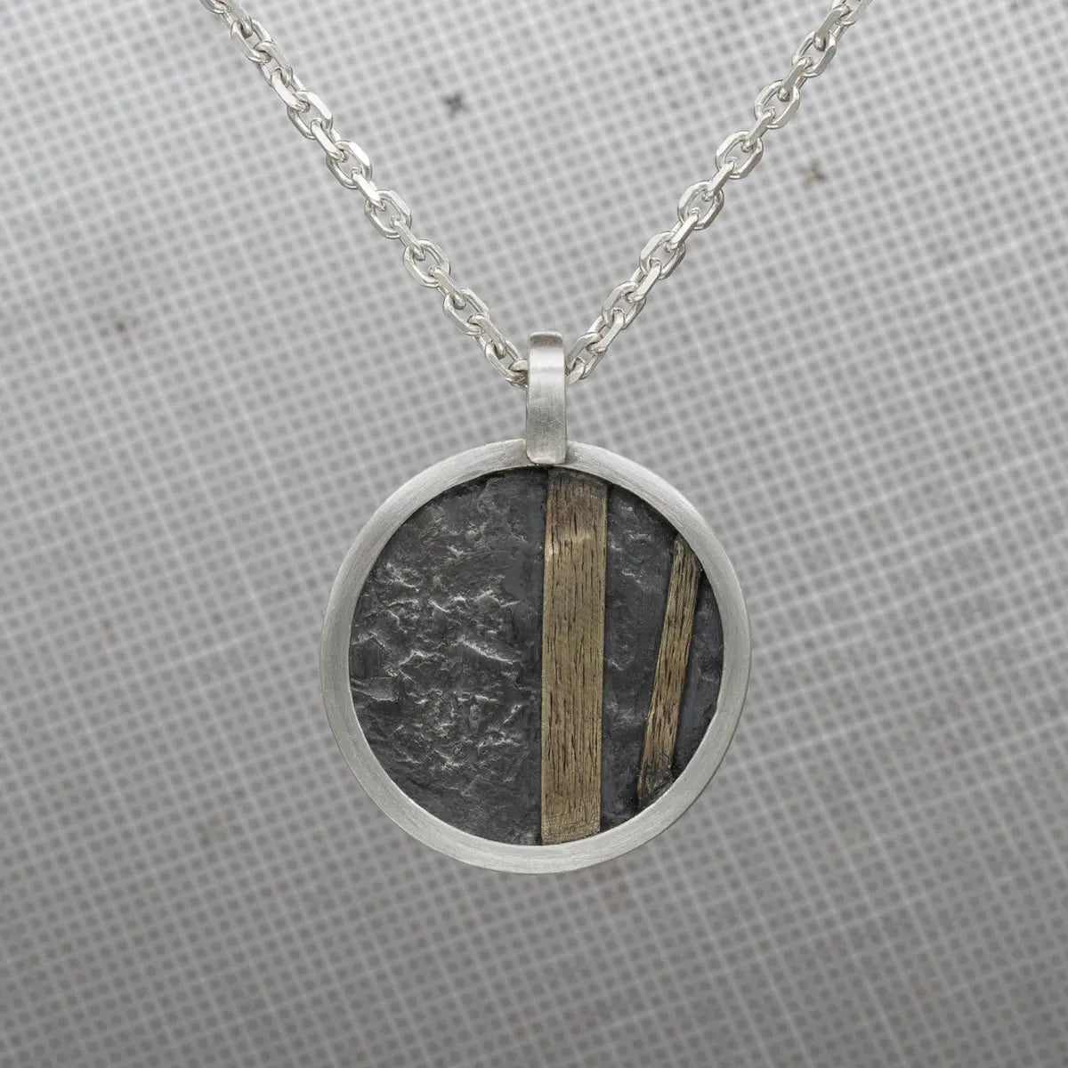 A circular pendant necklace with a geometric design, combining rugged stone texture and polished brass accents.