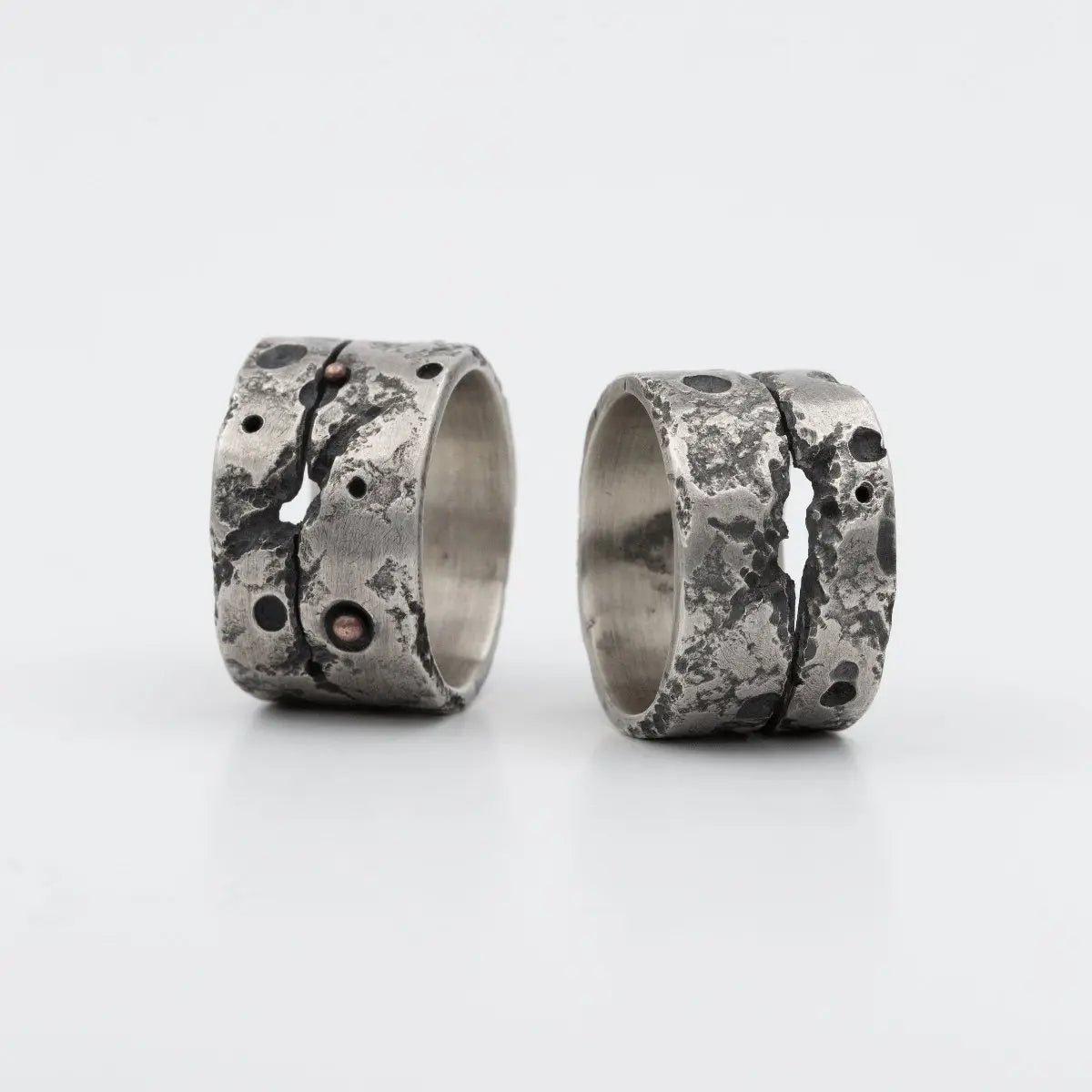 A pair of rugged, textured silver rings with distinctive crack-like designs and contrasting metallic accents.