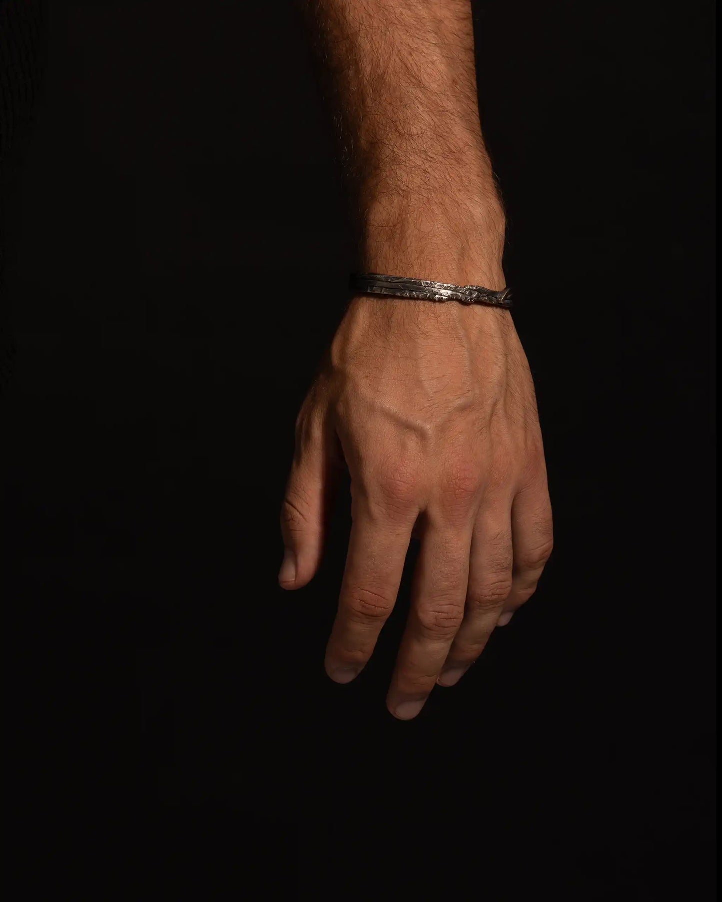 Hand wearing a handcrafted 925 silver Sativa bracelet with a rough texture and intertwined design.