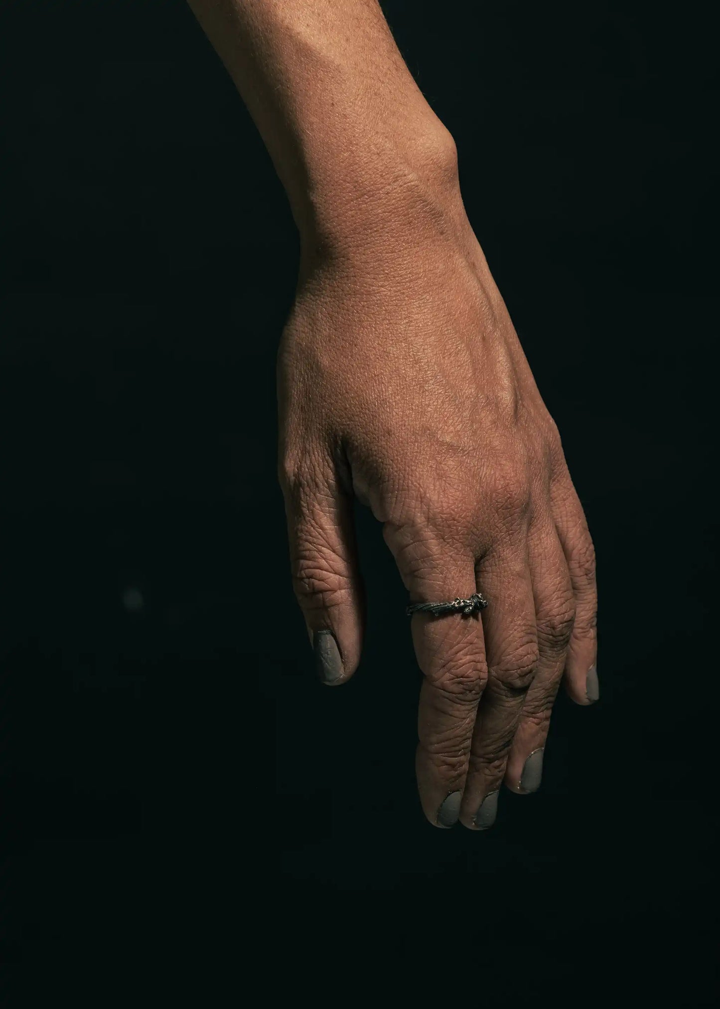 Sterling silver a close-up of a hand wearing an organic-style ring with intricate textures, set against a dark background.