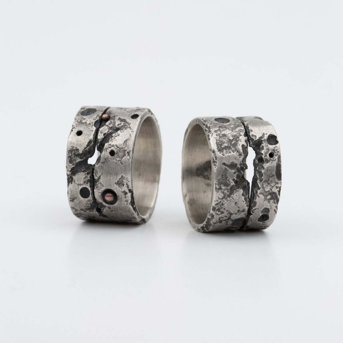 Close-up of two textured, handcrafted silver rings with rugged, organic details and subtle copper accents. A unique design inspired by natural imperfections.