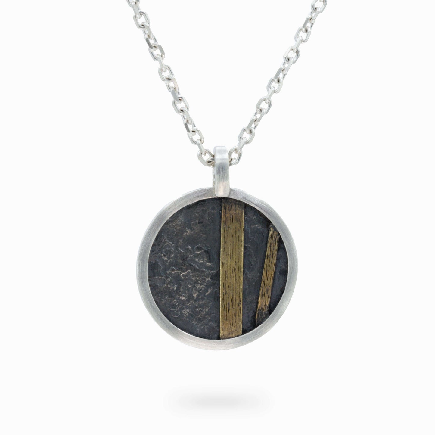 Round silver pendant with textured oxidized details and bold brass accents. A modern, artistic design symbolizing strength and individuality.