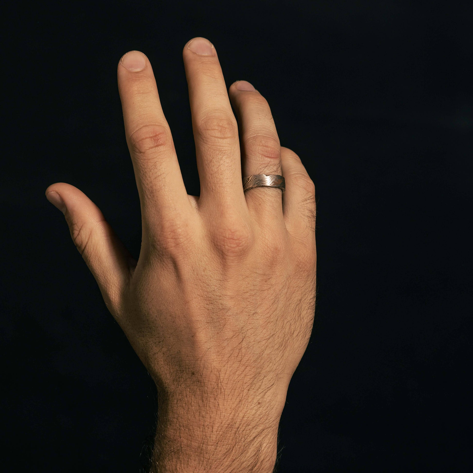 A hand wearing the Moku Ring, showcasing its natural, woodgrain-inspired pattern that merges earthy textures with refined craftsmanship.