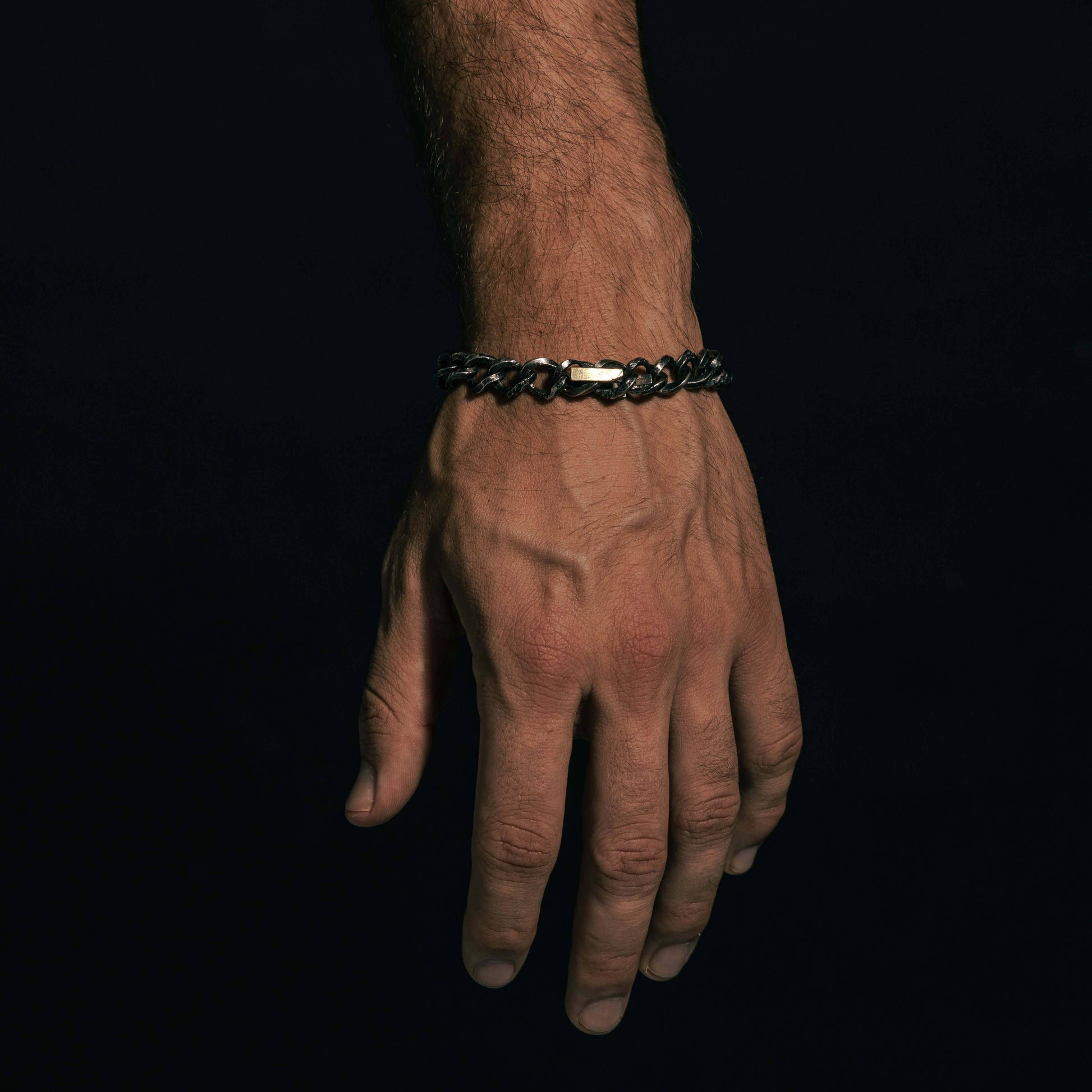 An oxidized silver bracelet with intricate links, showcasing a polished gold covered cross centerpiece for a striking contrast.