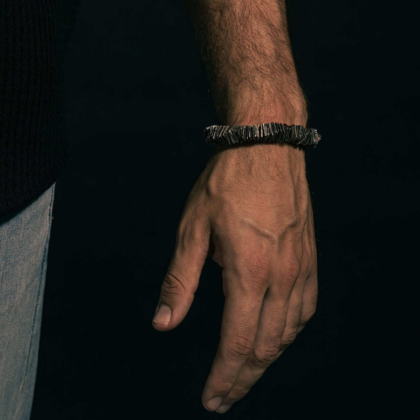 Hand wearing the 'Plates' bracelet, captured at an angle to highlight its layered silver detailing and rugged sophistication.