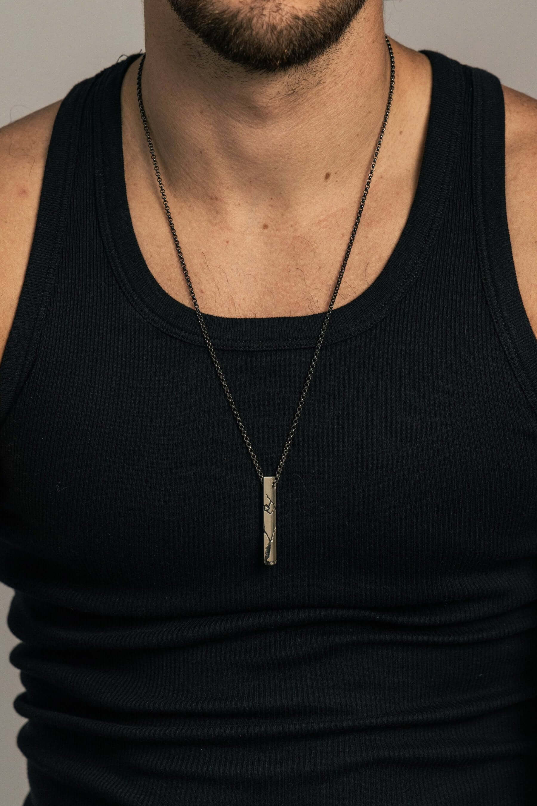 A man wearing a lightning-inspired pendant on a black chain, perfectly paired with a casual tank top. The pendant's rugged elegance adds a bold, modern touch to his look.