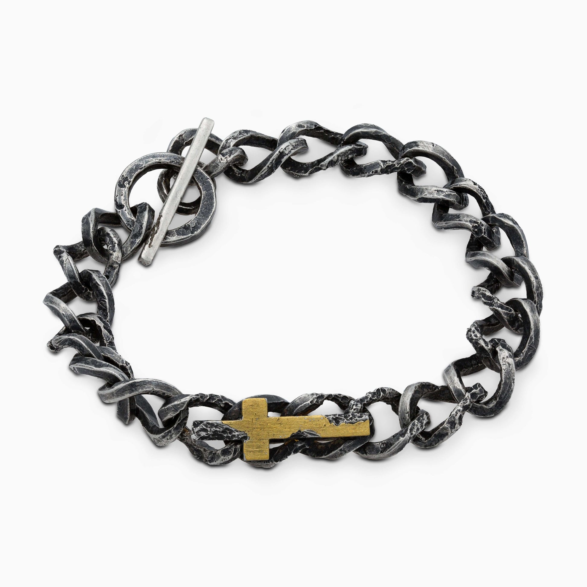 Close-up of a rugged silver bracelet with a toggle clasp, emphasizing the refined gold covered cross detail in its design.